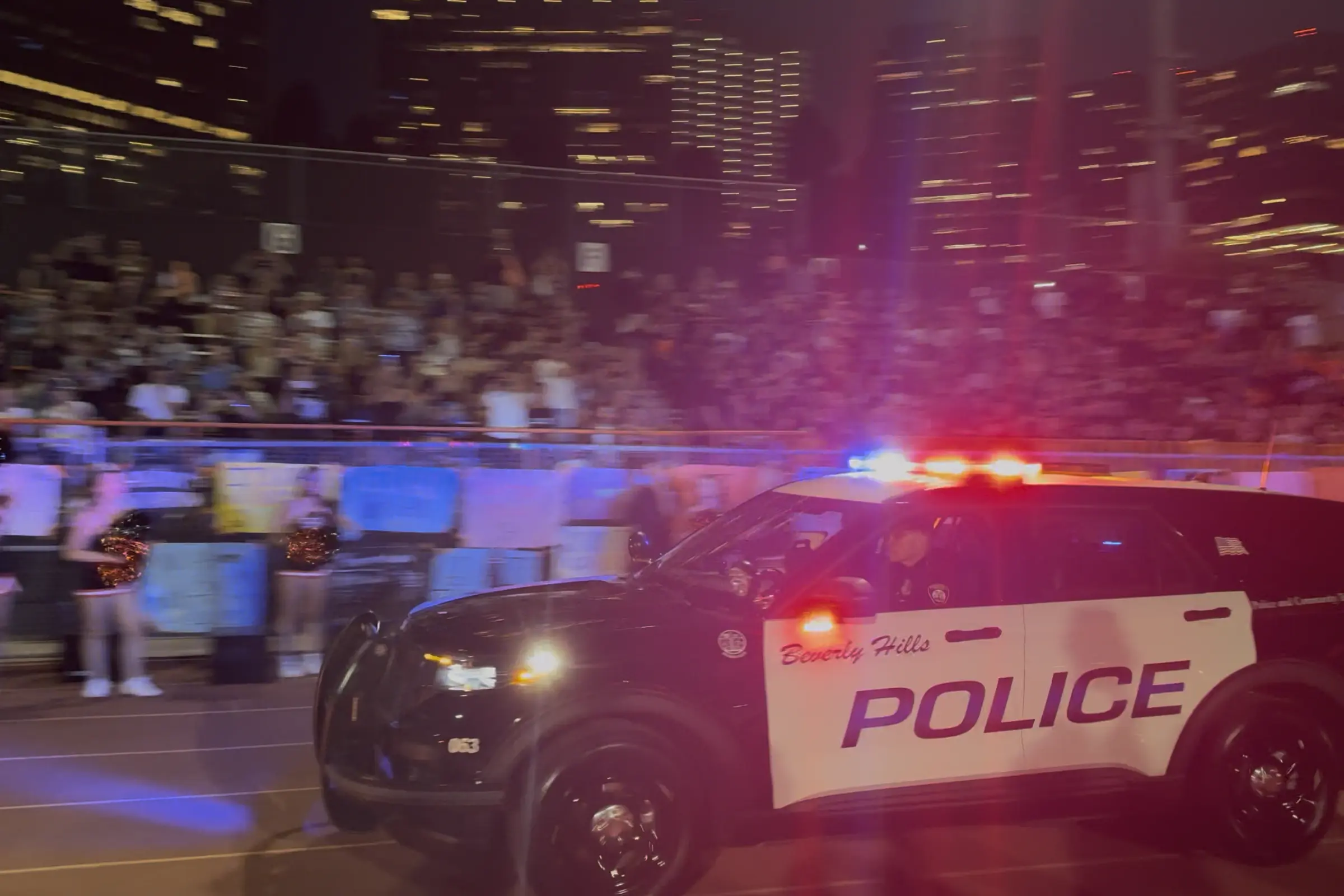 A Beverly Hills Police Department patrol vehicle circles the track with lights and sirens activated following a Norman touchdown, as fans cheer from the stands during BHHS' home opener.