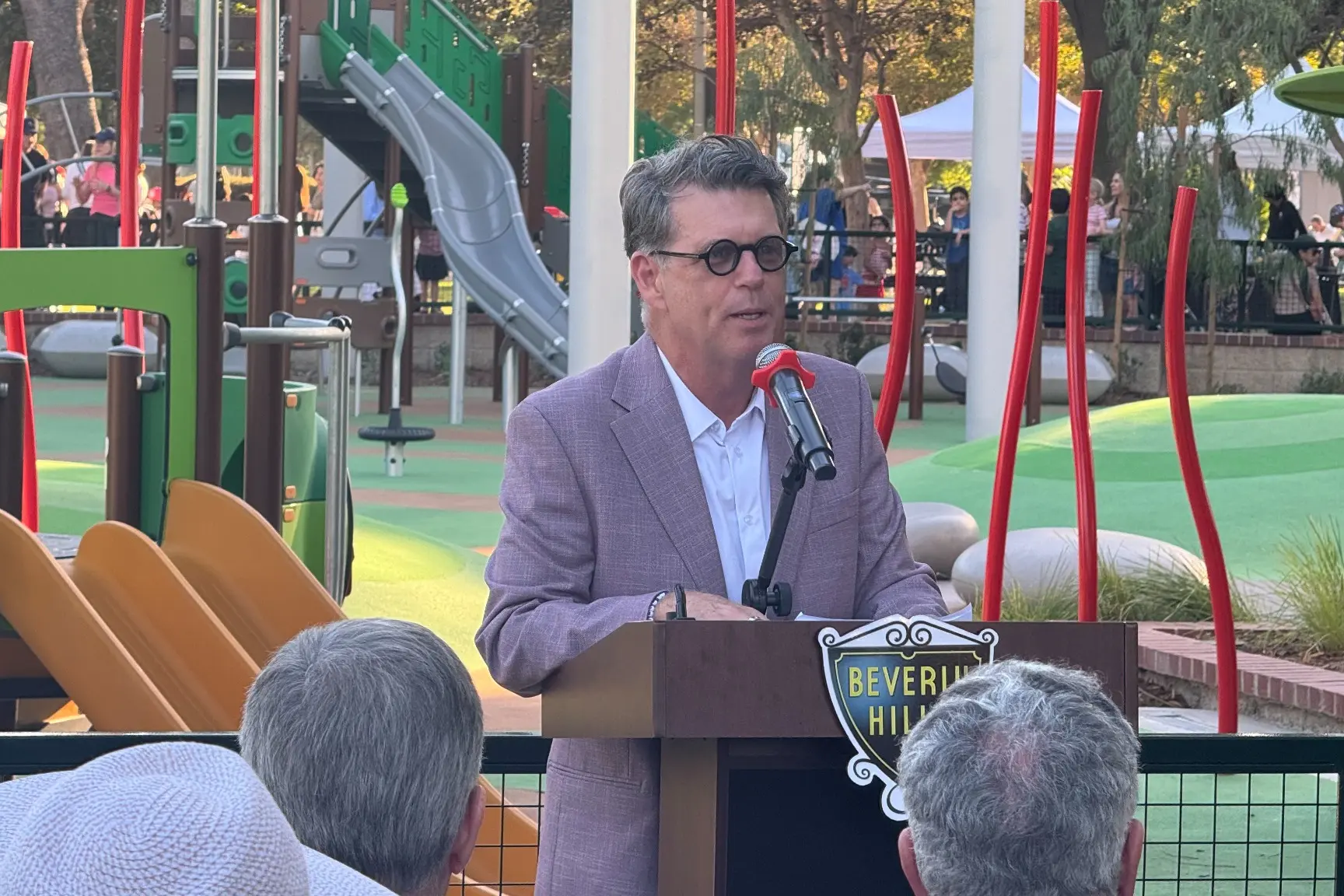 Recreation and Parks Commission Chair JR Dzubak speaks into a microphone at a Beverly Hills podium in front of the La Cienega playground.
