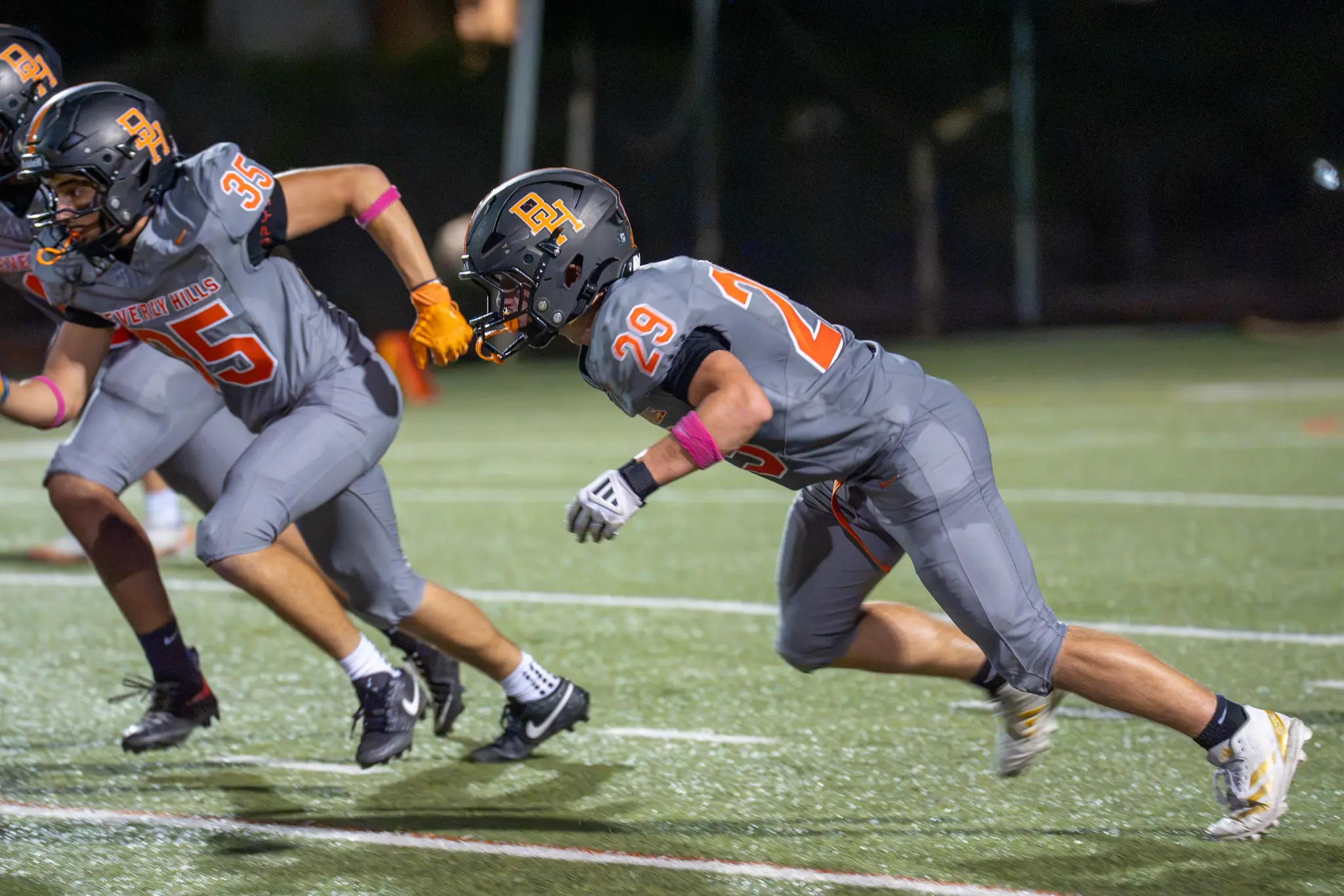 Beverly Hills football players wearing numbers 35 and 29 run across the field.