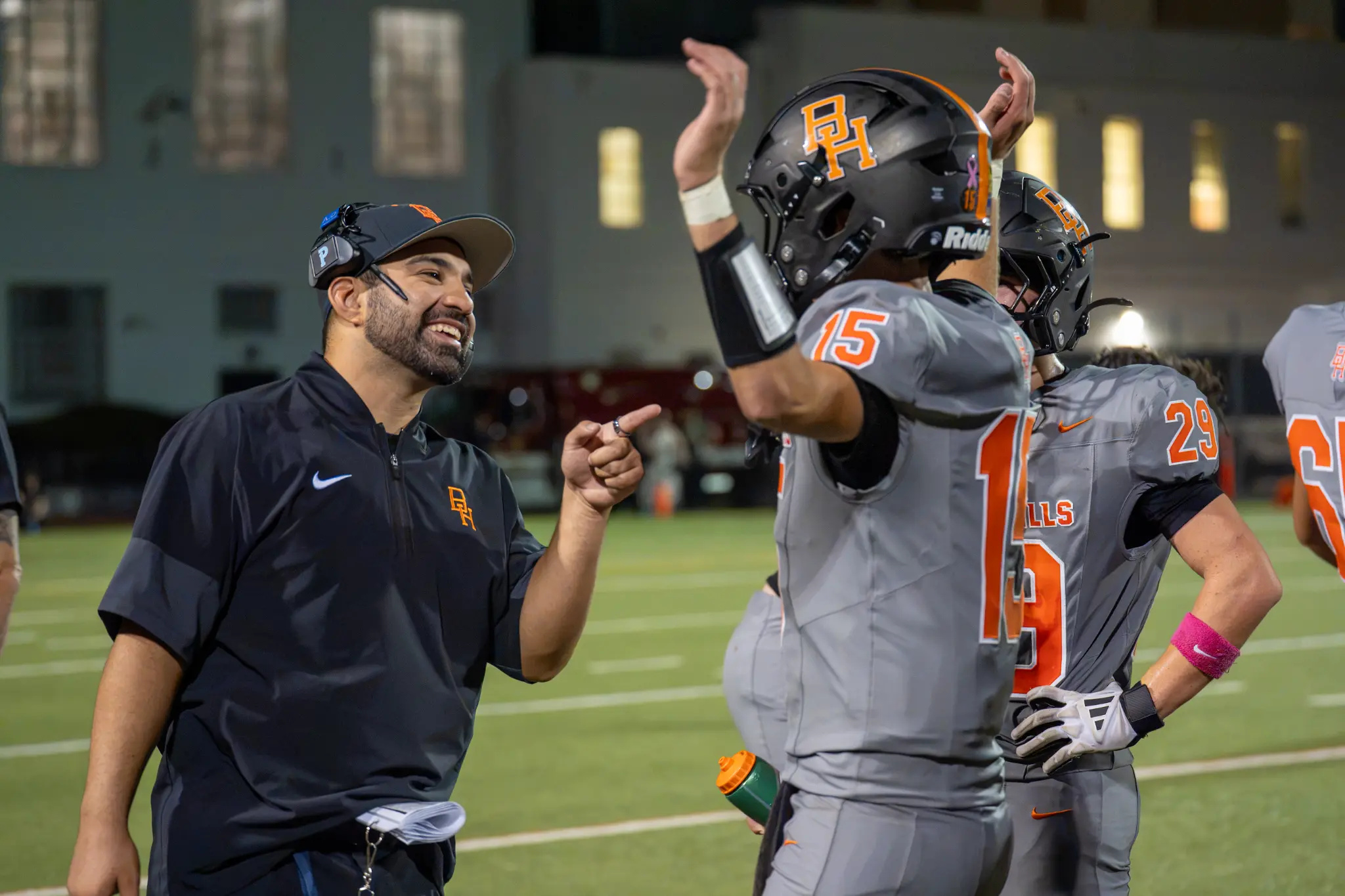 A smiling Beverly Hills coach stands beside football players, including a player raising his hands.