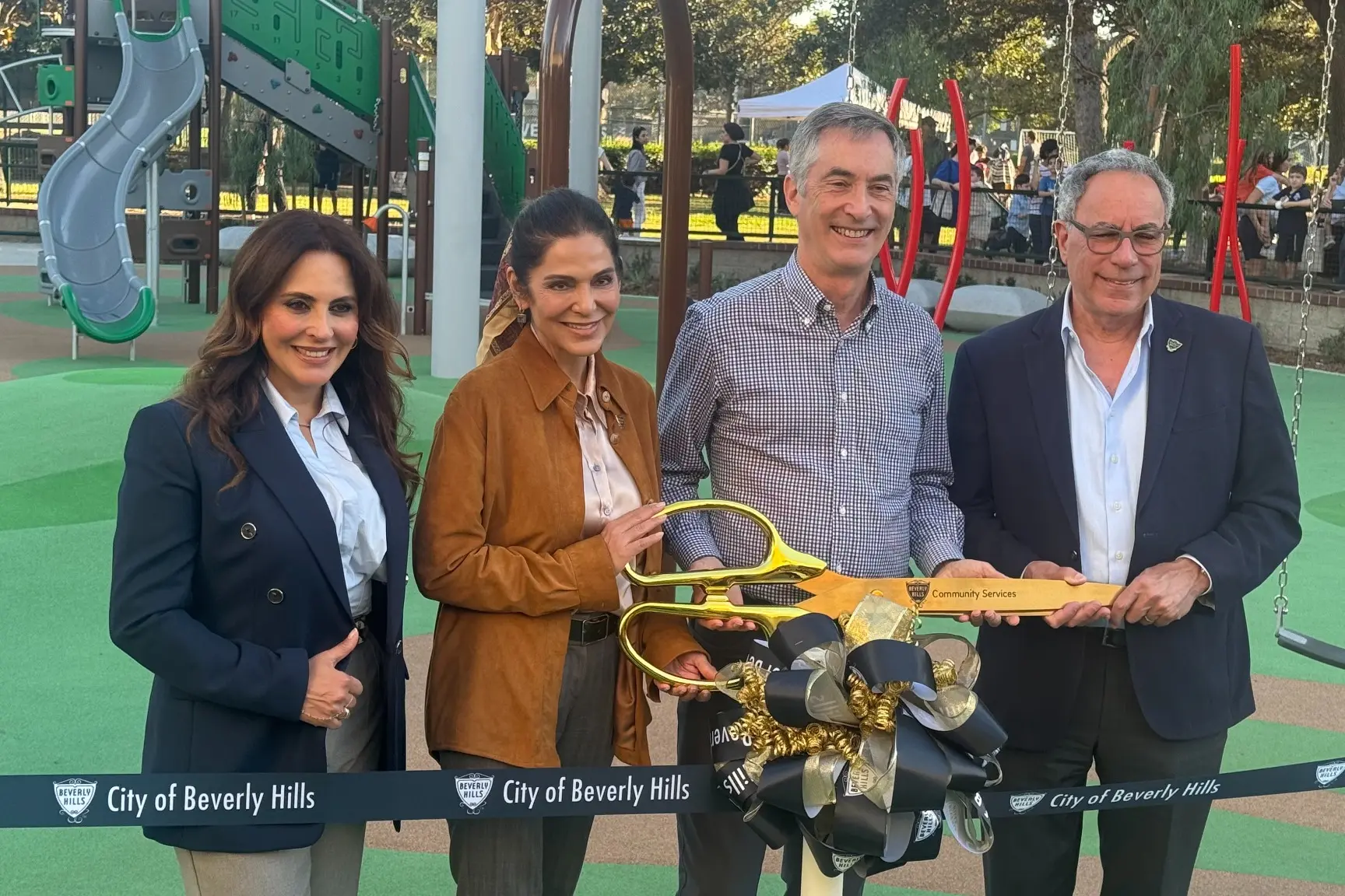 Sharona Nazarian, Mary Wells, Craig Corman and Lester Friedman stand together holding oversized gold scissors behind the ribbon at La Cienega Park.