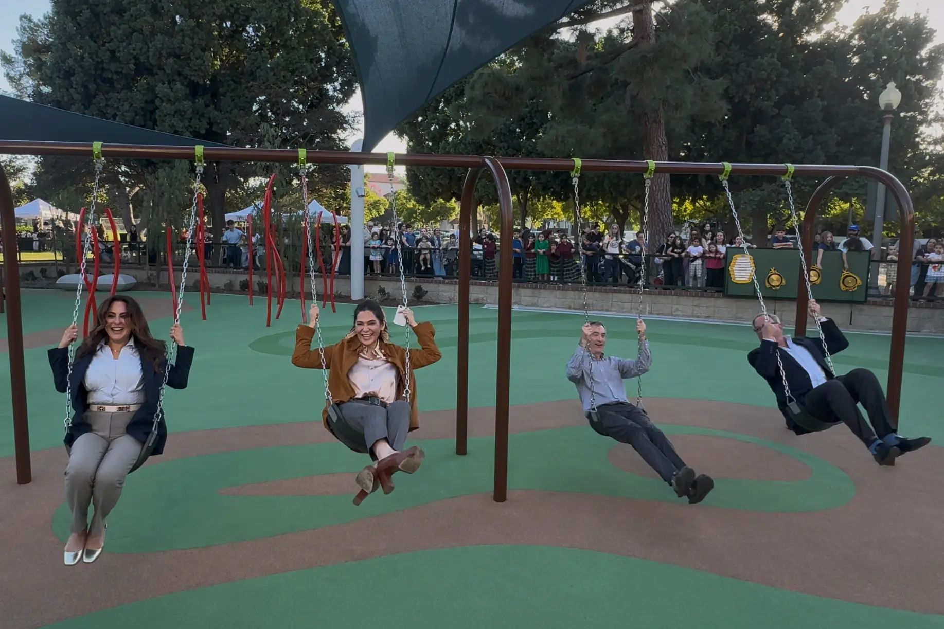 Sharona Nazarian, Mary Wells, Craig Corman and Lester Friedman, from left, ride four playground swings as families watch from behind the fence.