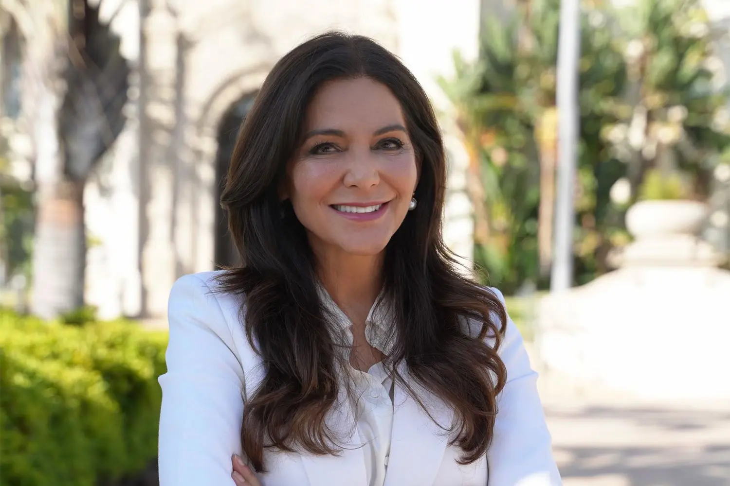 Mary Wells in a white blazer outdoors, smiling with her arms crossed.