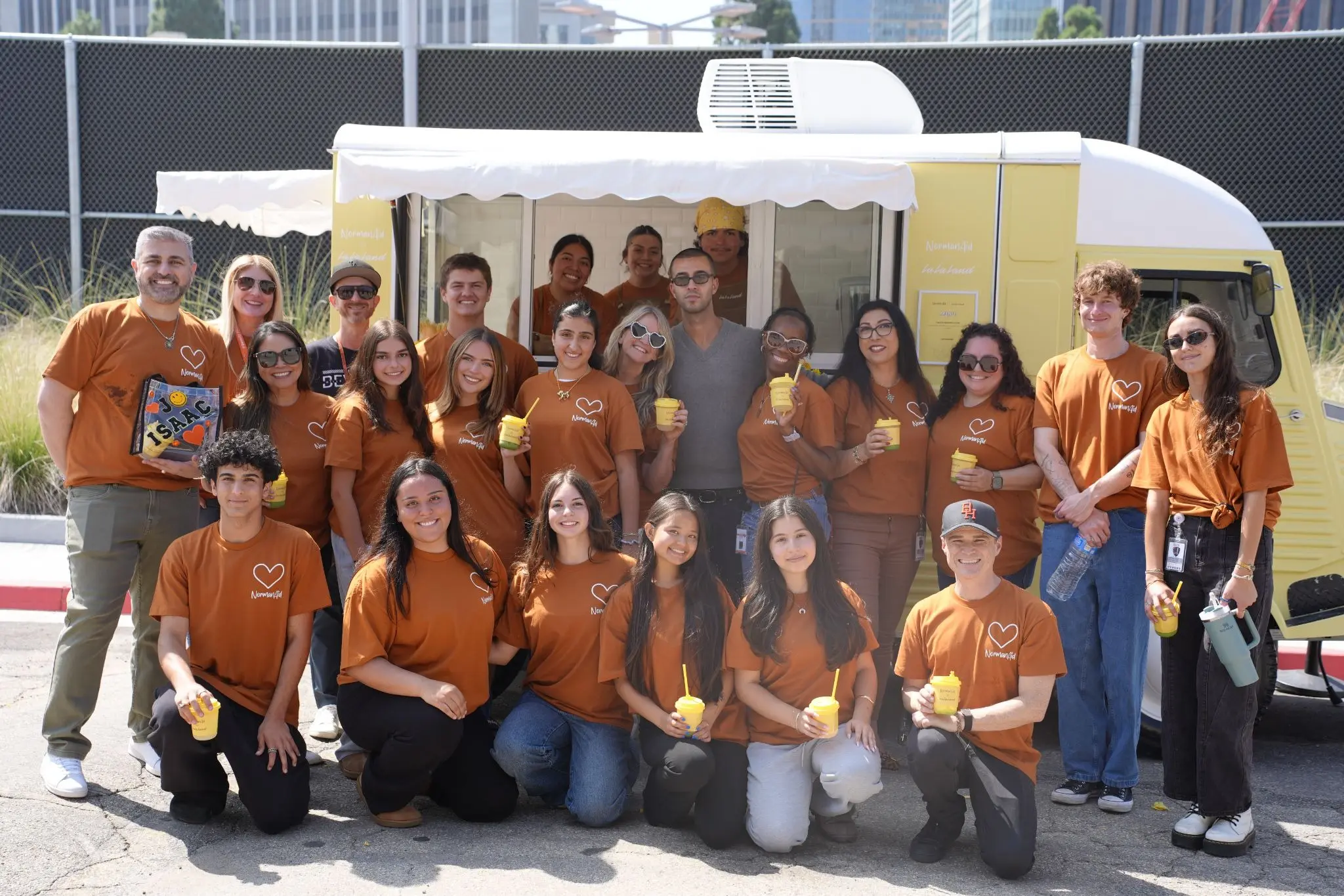 A group wearing NormanAid shirts gathers beside a yellow La La Land Cafe truck.