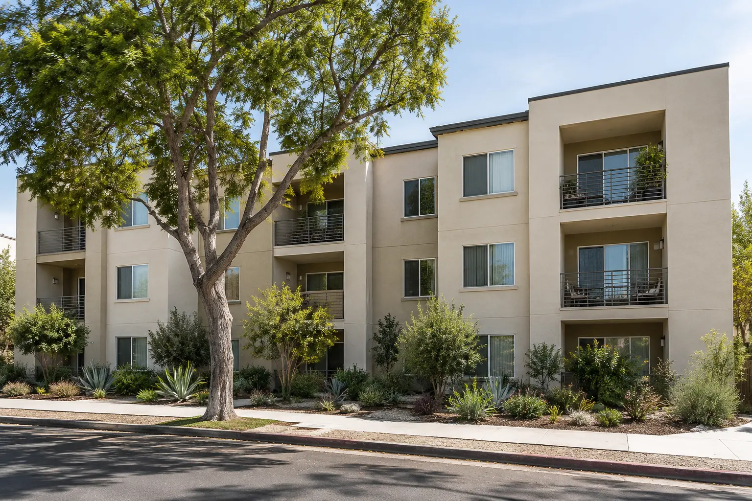 Photographic illustration of a three-story stucco apartment building with balconies, landscaping and a sidewalk.