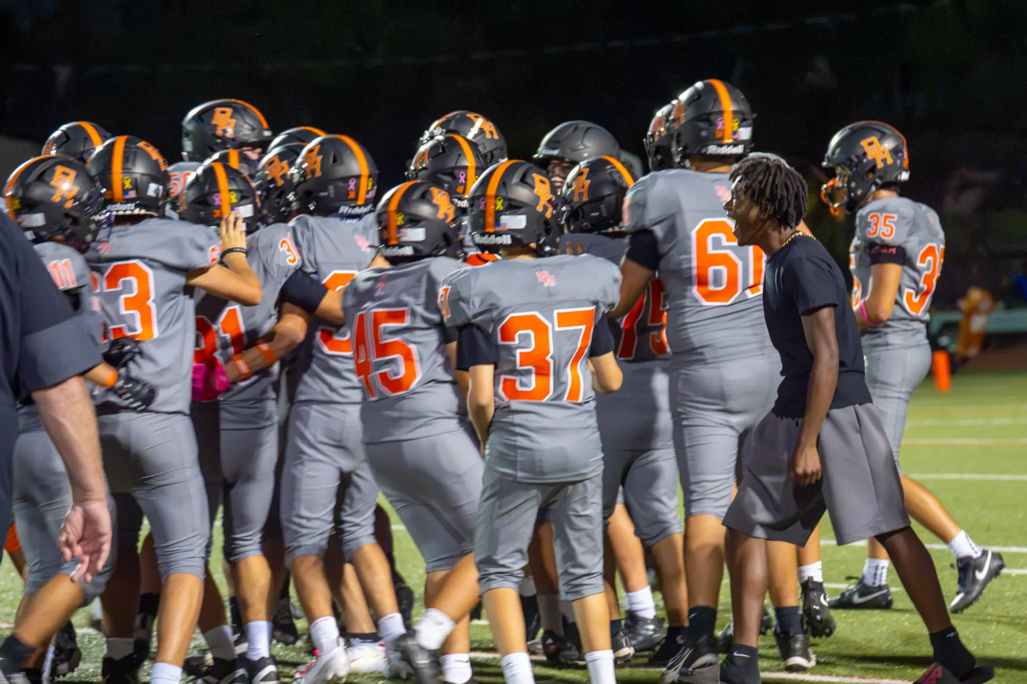Beverly Hills High School football players gather on the field in gray uniforms and black helmets.