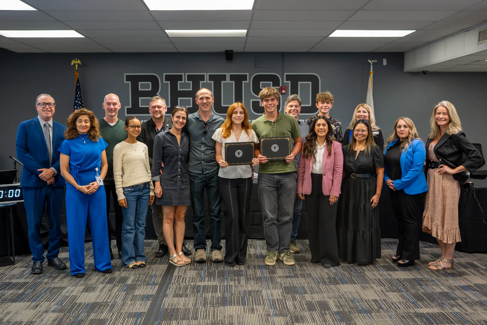 BHHS National Merit Semifinalists pose with certificates alongside family members and district representatives in the BHUSD boardroom.