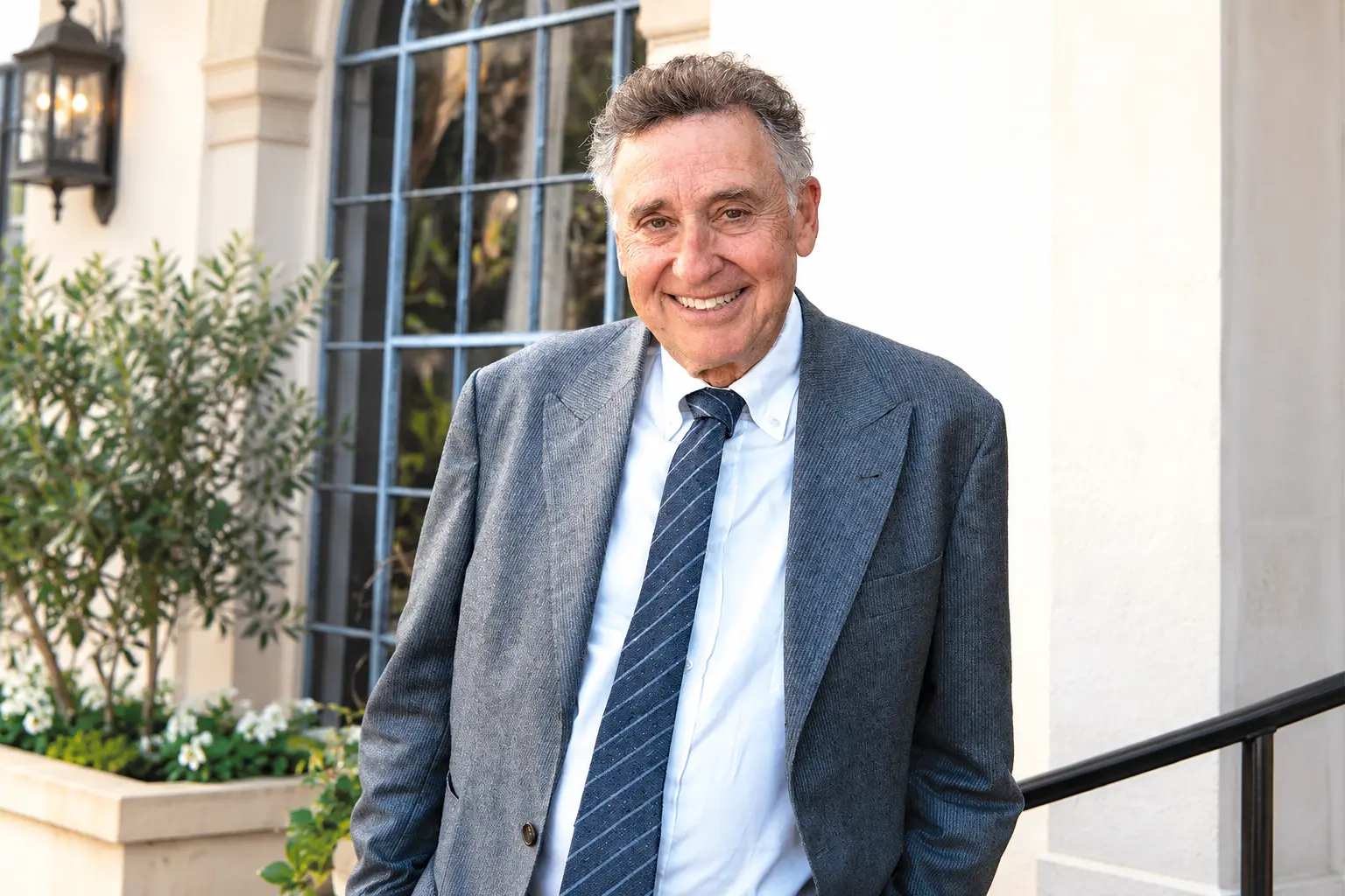 Andy Licht wearing a gray blazer, white shirt and blue striped tie, smiling outside a building.