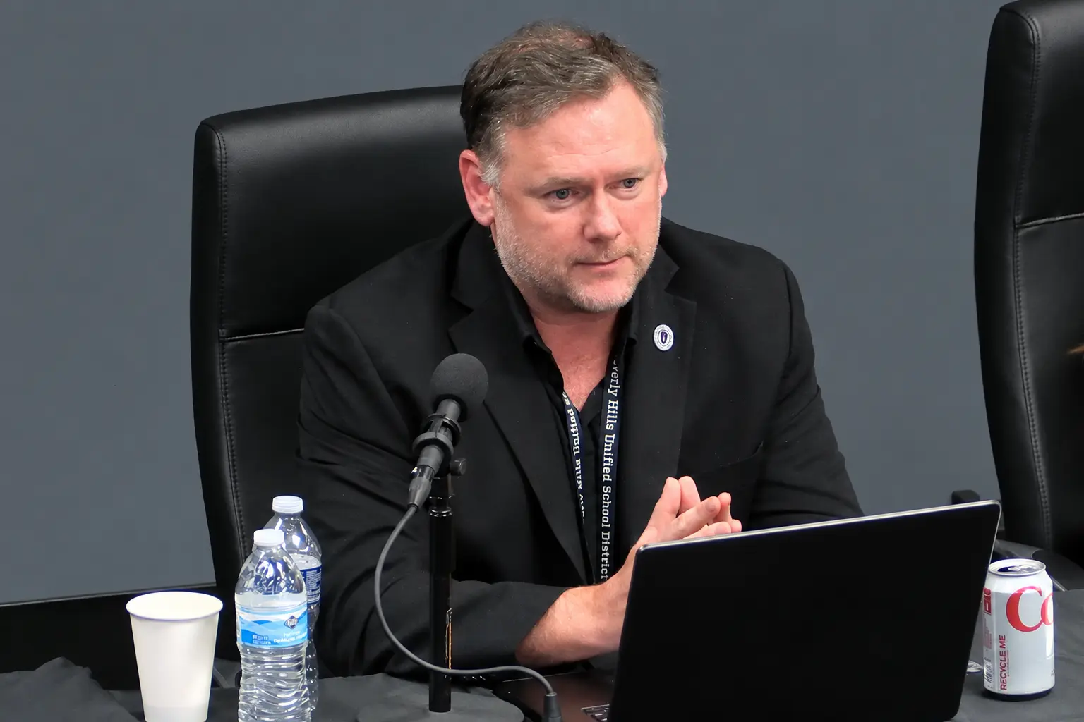 Russell Stuart seated at a board meeting table, speaking into a microphone.