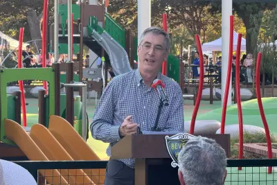 Mayor Craig Corman speaks at a Beverly Hills podium with the renovated La Cienega playground behind him.