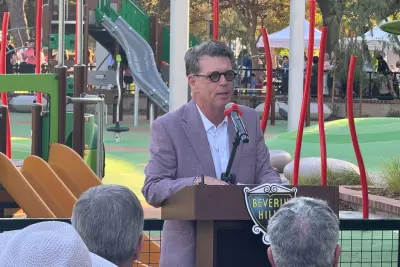 Recreation and Parks Commission Chair JR Dzubak speaks into a microphone at a Beverly Hills podium in front of the La Cienega playground.